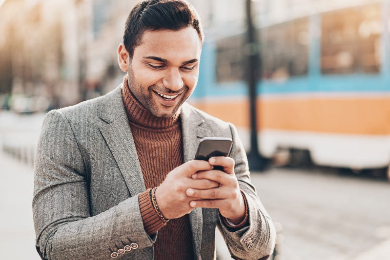 Man standing on sidewalk looking at his phone and smiling