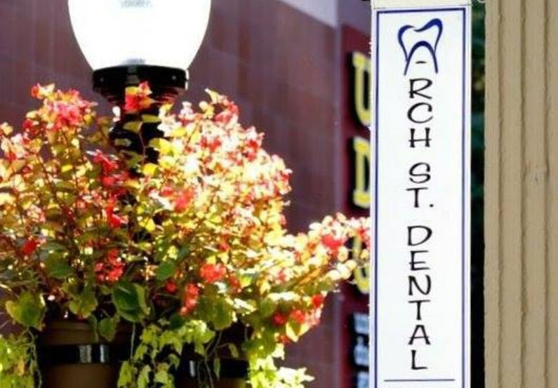 View of the side of Arch street dental with a red flowering plant hanging from a lampost
